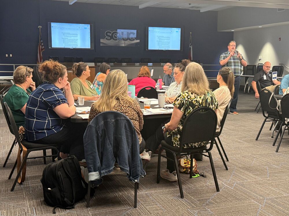 SCUC ISD staff and community members participate in a collaborative meeting in the district board room while a presenter speaks at the front of the room.