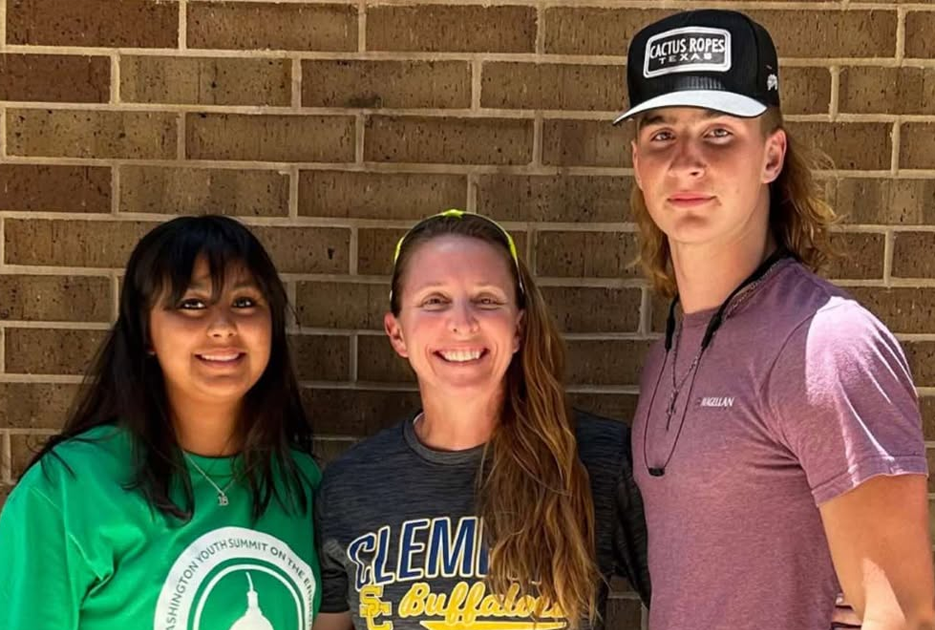 a high school science teacher flanked by two students stands before a brick wall