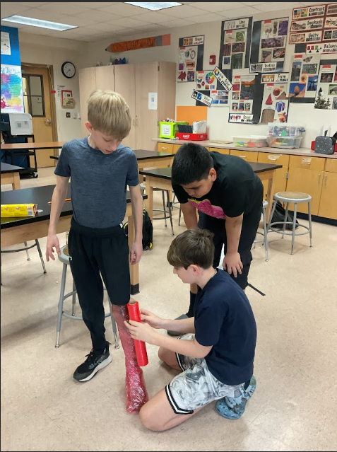 A group of boys using saran wrap around a leg to create 3d sculptures.