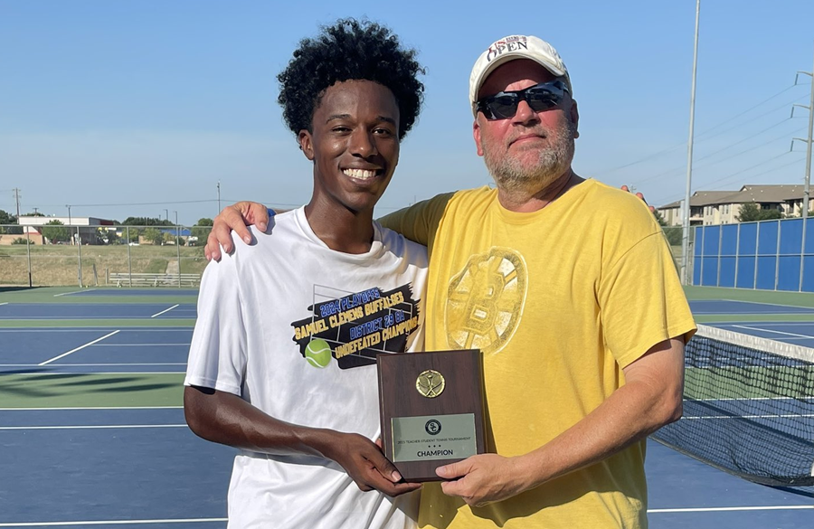 student & teacher stand next to each other on a tennis court clutching a champion trophy