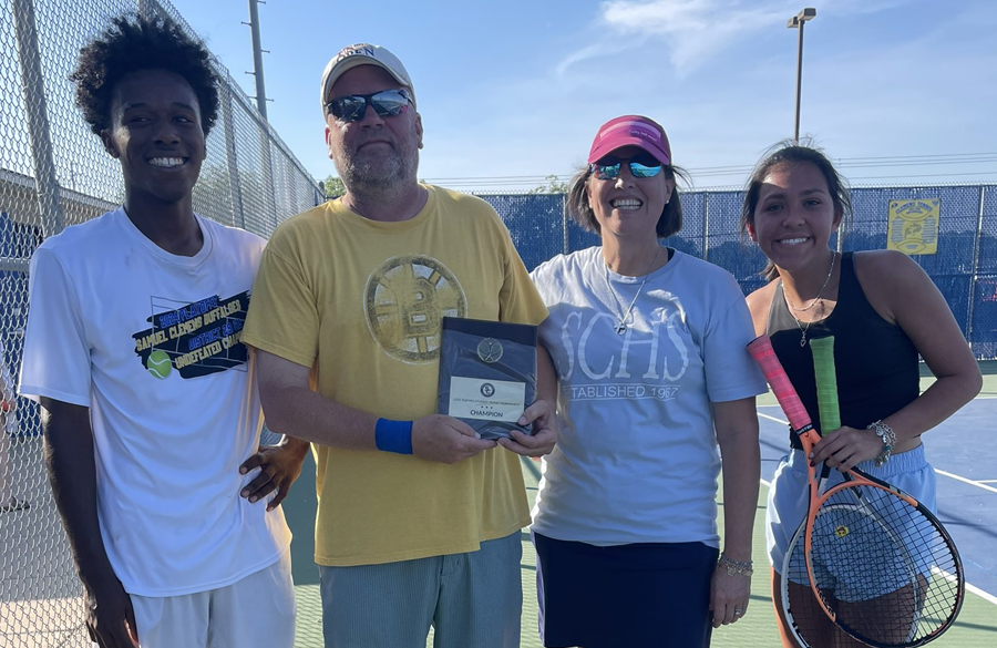 students & teachers smile for the camera on a tennis court holding a trophy and tennis rackets