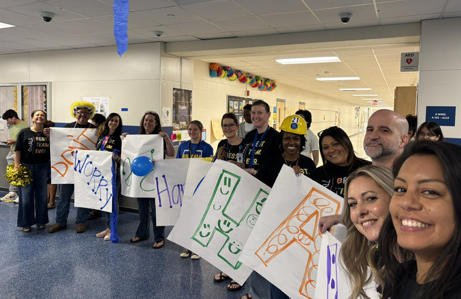 counselors & frontline staff line a high school hallway while clutching signs & posters that spell out "don't worry, be happy"