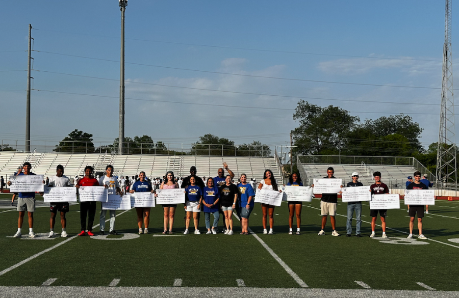 student athletes stand on a football field beneath a blue sky holding giant mock checks