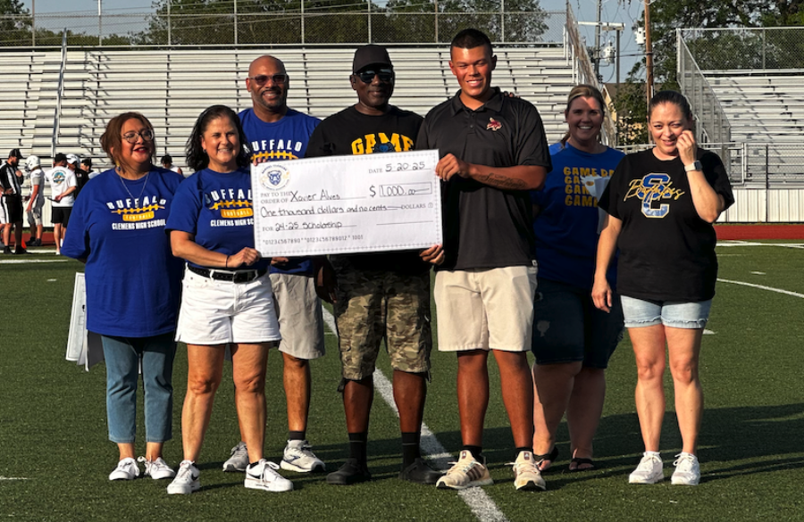 student athlete & adults stand on a football field beneath a blue sky holding giant mock check