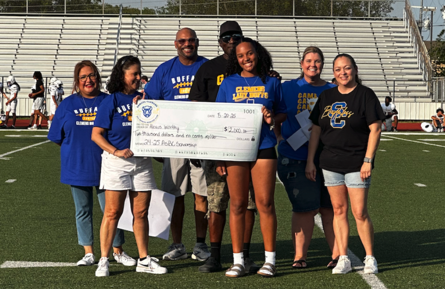 student athlete & adults stand on a football field beneath a blue sky holding giant mock check