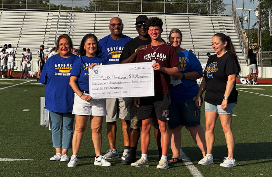 student athlete & adults stand on a football field beneath a blue sky holding giant mock check