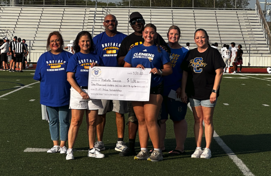student athlete & adults stand on a football field beneath a blue sky holding giant mock check