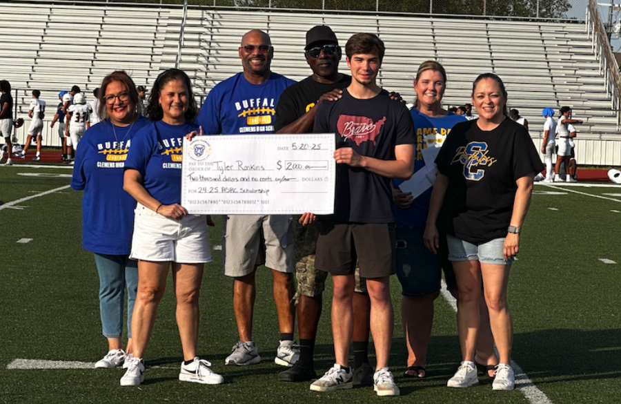 student athlete & adults stand on a football field beneath a blue sky holding giant mock check
