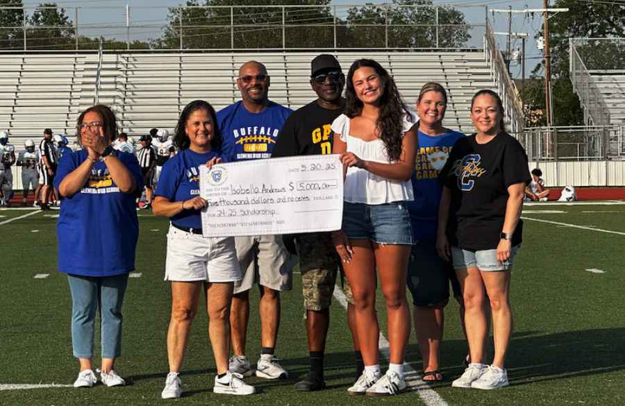 student athlete & adults stand on a football field beneath a blue sky holding giant mock check