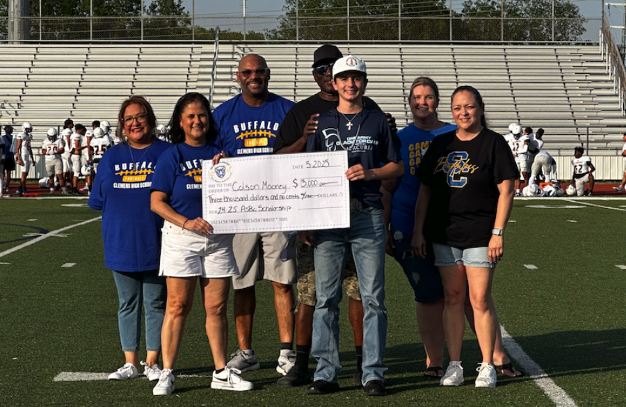 student athlete & adults stand on a football field beneath a blue sky holding giant mock check