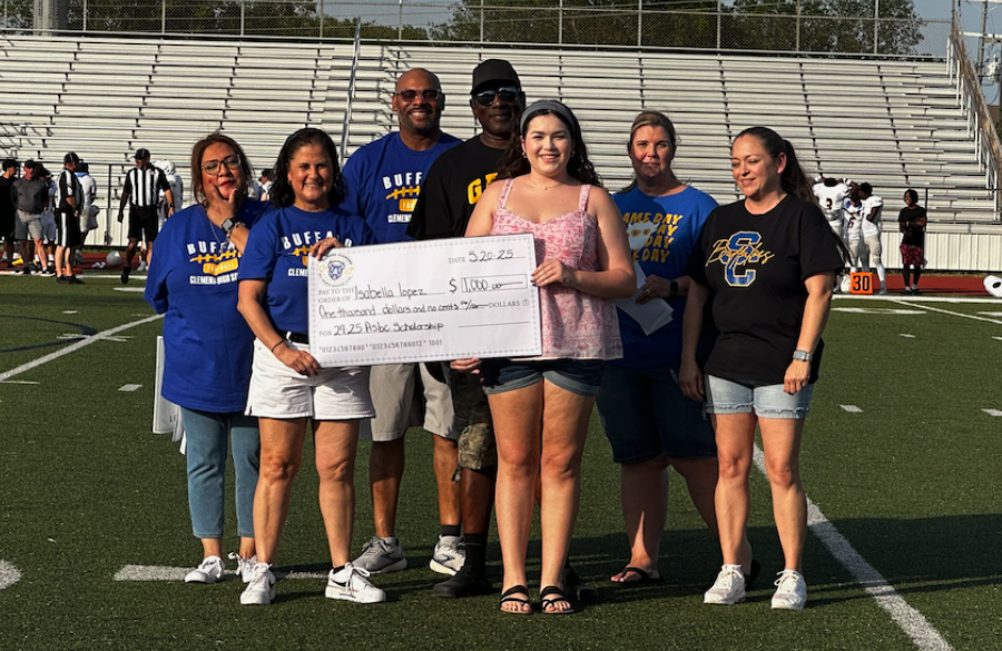 student athlete & adults stand on a football field beneath a blue sky holding giant mock check