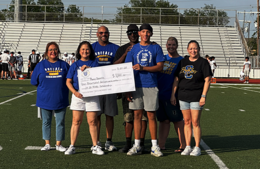 student athlete & adults stand on a football field beneath a blue sky holding giant mock check