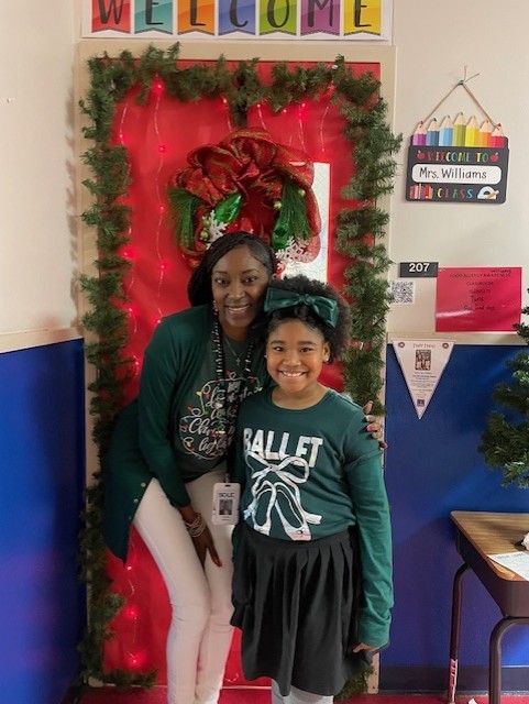 Elementary school teacher posing with student in front of holiday decorated door in the classroom.