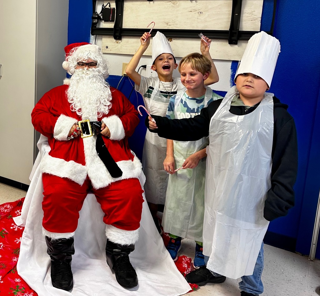 students holding candy canes and smiling posing for a picture standing next to someone dressed in a Santa costume