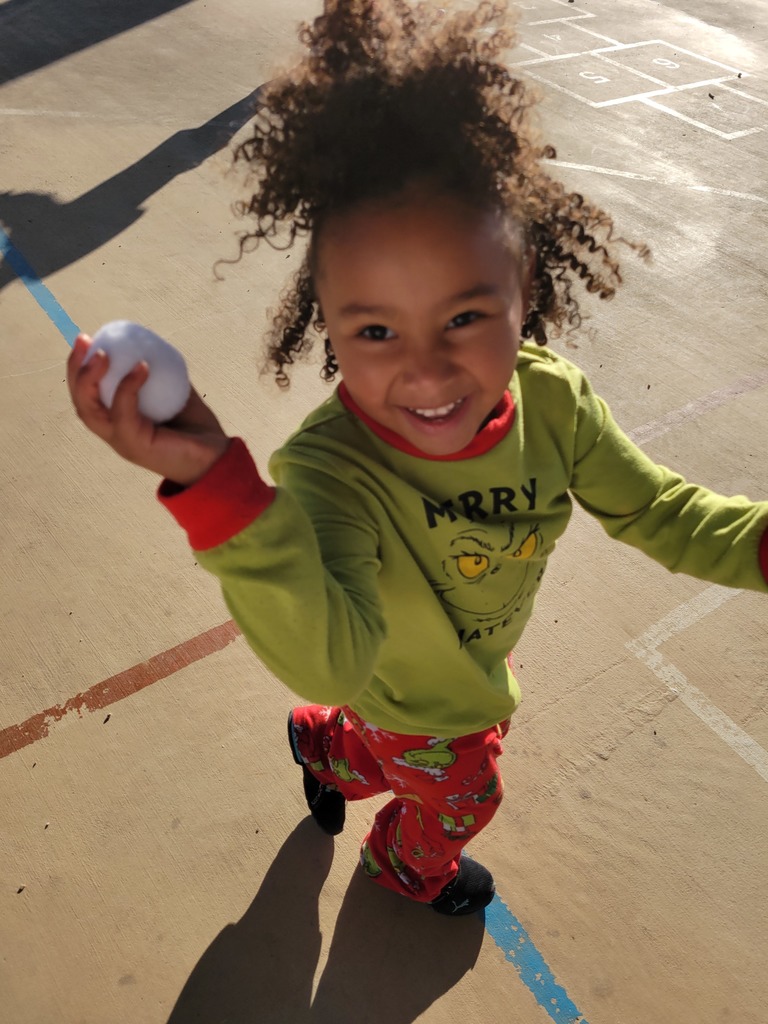 student wearing character pajamas running with a white soft ball in her hand.