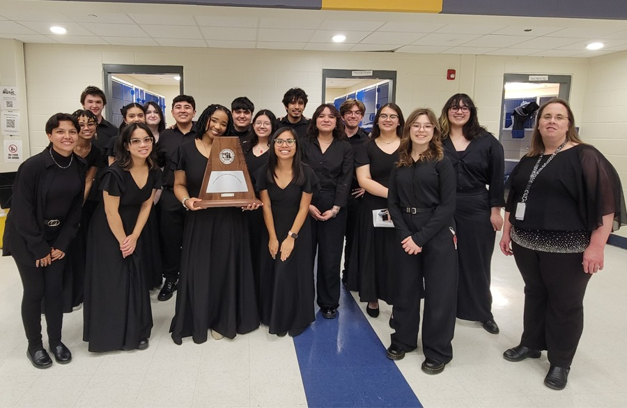 high school students & teacher, all clad in black, stand in high school classroom smiling for the camera & clutching a 1st place trophy