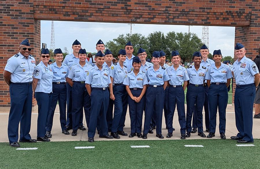 afjrotc cadets & instructors stand in short-sleeve usaf uniforms on a turf surface before a brick archway