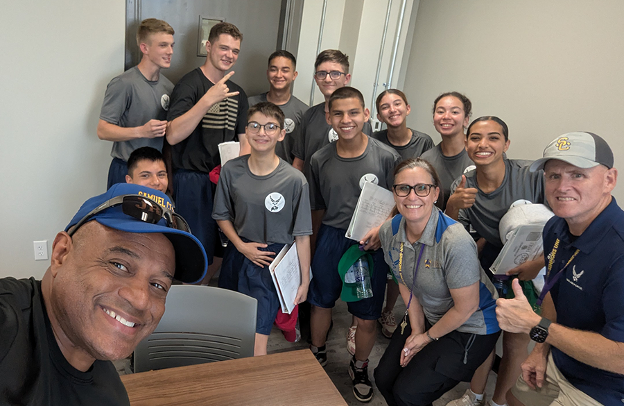 afjrotc cadets & instructors in athletic attire hunch to squeeze into frame inside a classroom