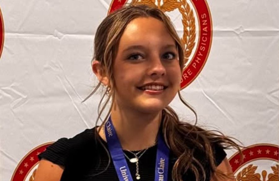 a female high school student in a black blouse stands before a white backdrop emblazoned with logos for the congress of future medical leaders