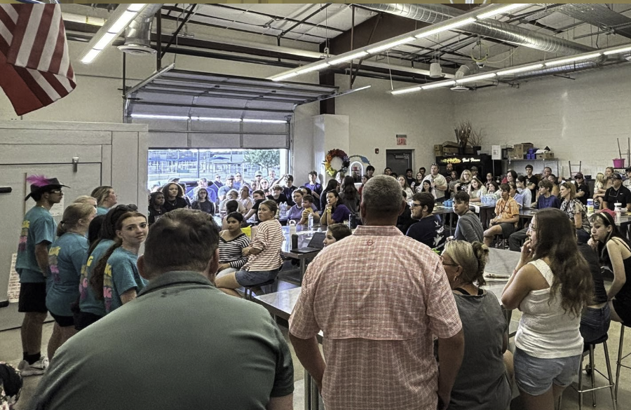 adults & students stand in a garage-style classroom 