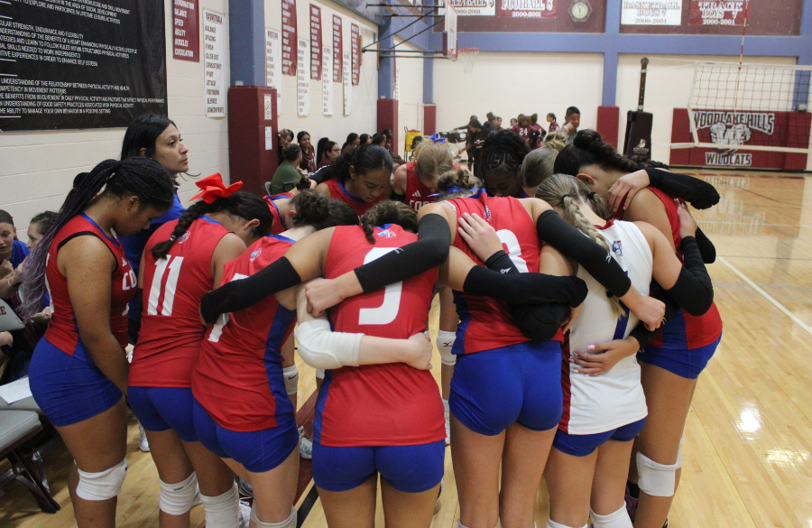 A huddle of volleyball players and Coach Ramirez  in a circle