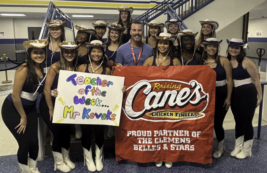clemens dancers in uniform surround mr. kovacs in the mall area of clemens high school, holding signs reading "teacher of the week...mr. kovacs" & "raising cane's chicken fingers, proud partner of thge clemens belles & stars"