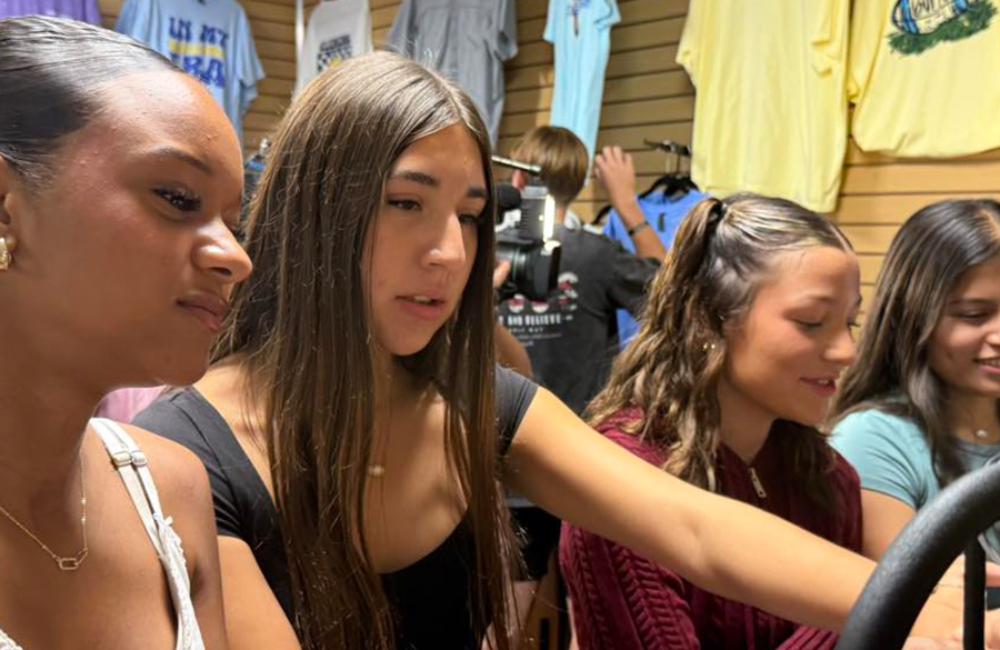 high school students browse a rack of clothing inside of a student store with a news camera visible behind them