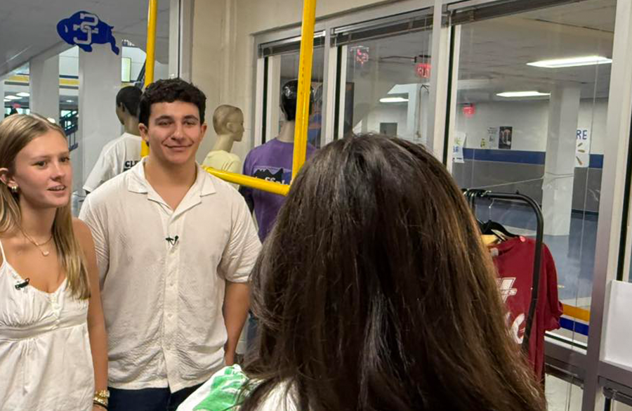 students talk with a news reporter inside of a glass-walled student store