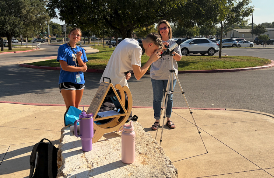 high school students make use of a special telescope for observing the sun in a parking lot; a science teacher gleefully looks on