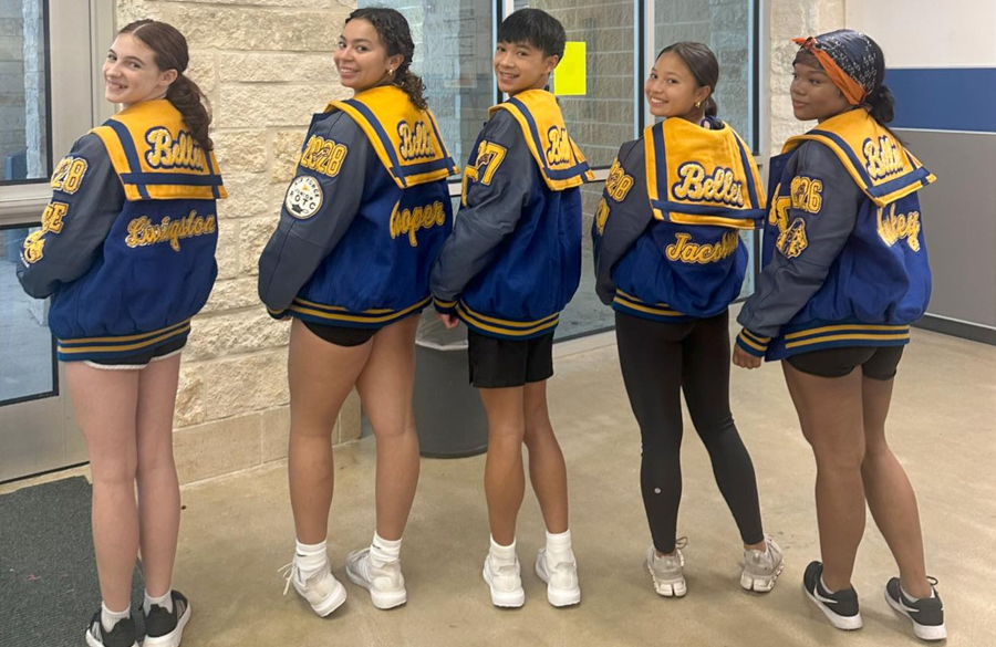 five high school dance team members wear blue & gold letterman jackets. each jacket has a small cape with "belles" stitched in a cursive script font
