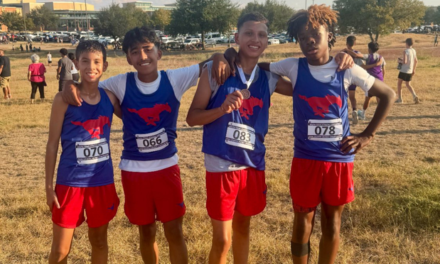A group of four boys cross country athletes at a meet, one showing his medal