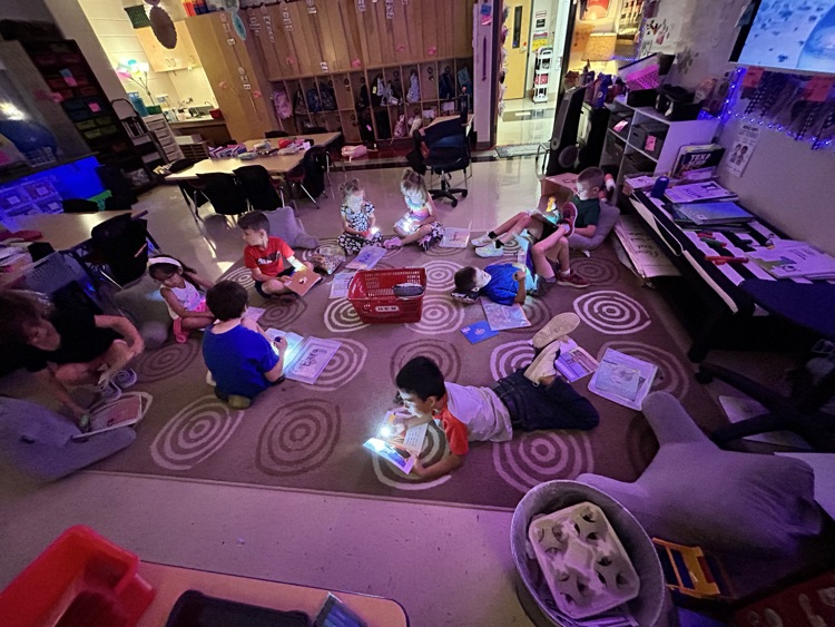 first grade students reading with flashlights in class