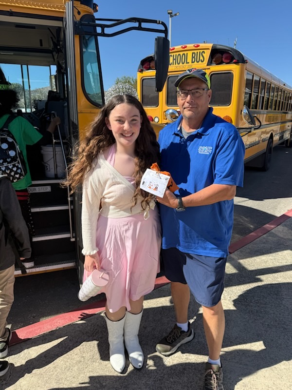 A student dressed up in a Halloween costume standing with a bus driver in front of a bus