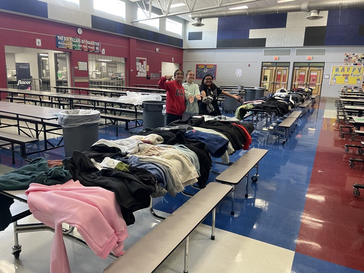 three students with the four tables of jackets in the cafeteria