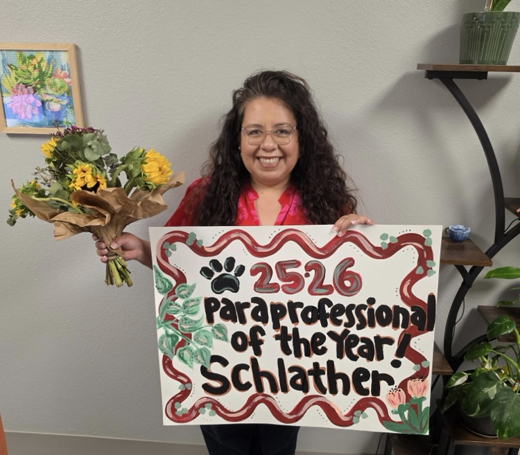 Mrs. Adam’s with a bouquet of flowers and a para of the year banner
