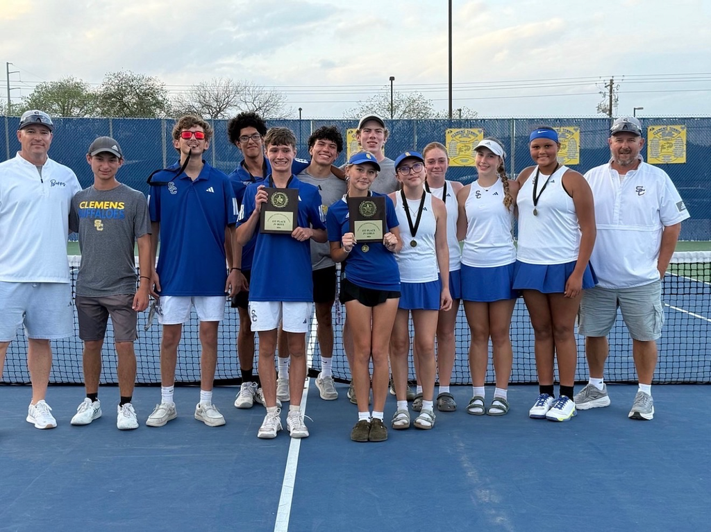 clemens high school jv tennis team stands on a tennis court, showing off 1st place trophies