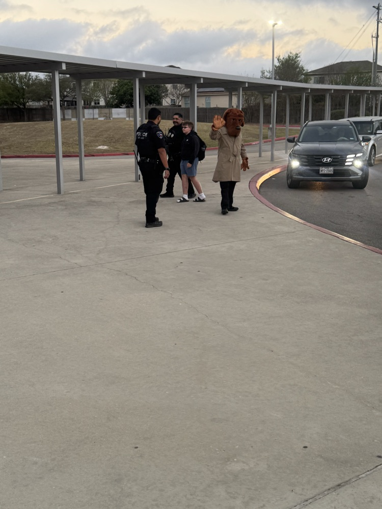 Police officer and watch dog mascot waving to students as they come to school