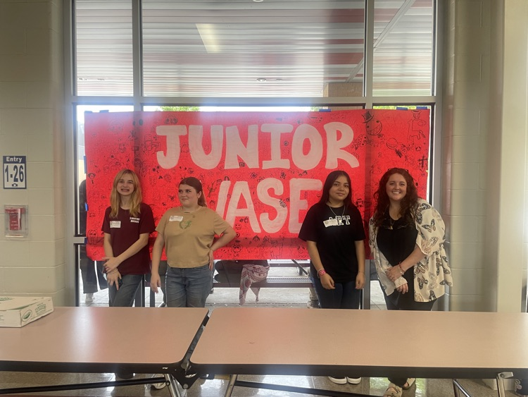 three girls and Miss Tucke posing in front of a junior vase poster