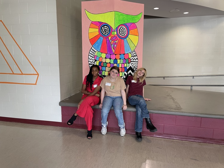 Three girls posing in front of a neon owl mural