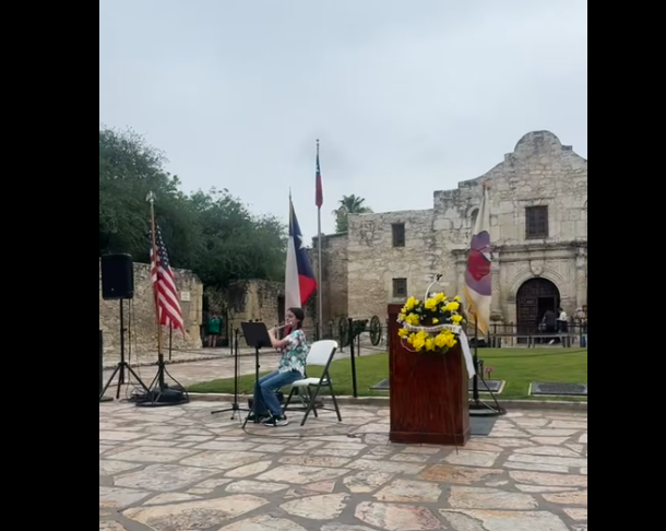 Jewel playing her flute infront of Texas flag and Alamo