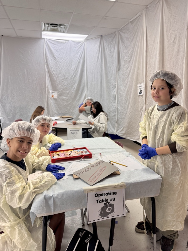 Students are smiling and posing at a table while they work on their review in operating costumes