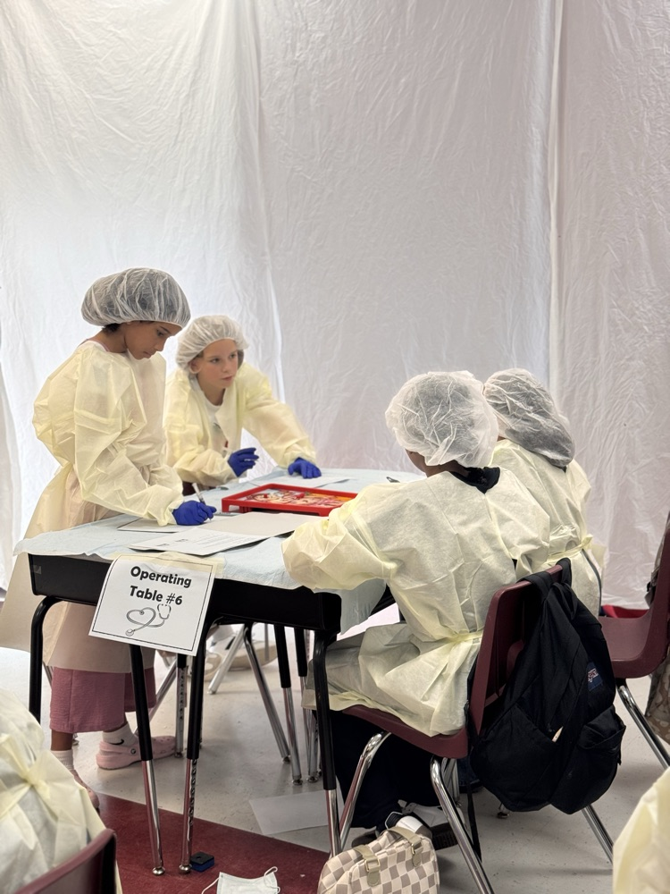 Students sitting at a table wearing operating costume costumes talking with each other