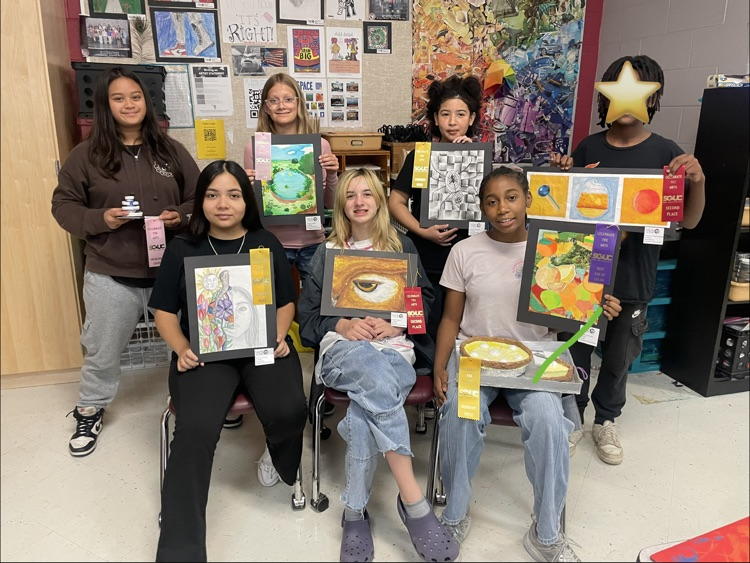 7 students gathered while holding up their artwork and ribbons 