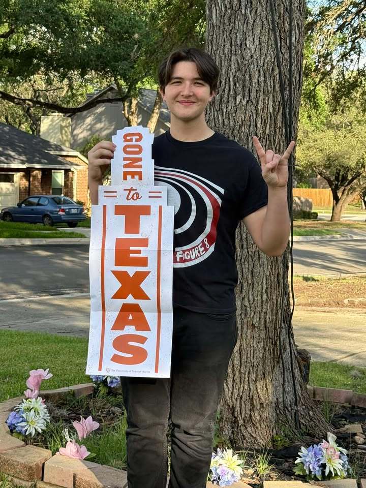 a high school student stands before  a large tree, holding a sign that reads "gone to texas" and making the longhorn symbol with his hands (a fist with index & pinky fingers extended)