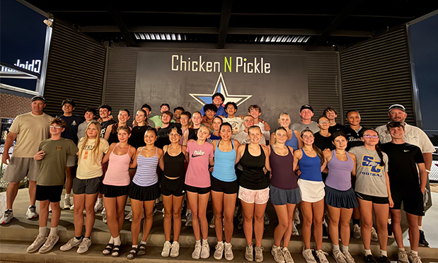 high school tennis team in casual wear stands before a stage at chicken n pickle