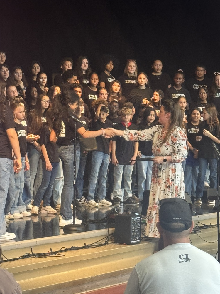 Miss Alvarado shakes a student hand, giving an award while the students stand behind her