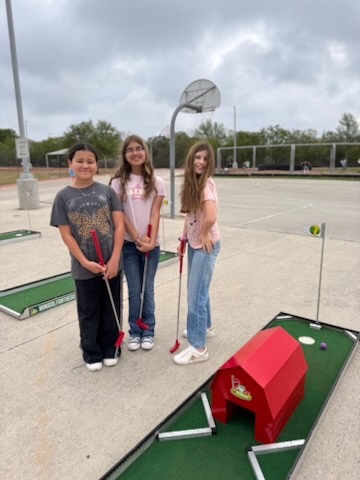 Students golfing on a mini golf course outside with a red barn on it