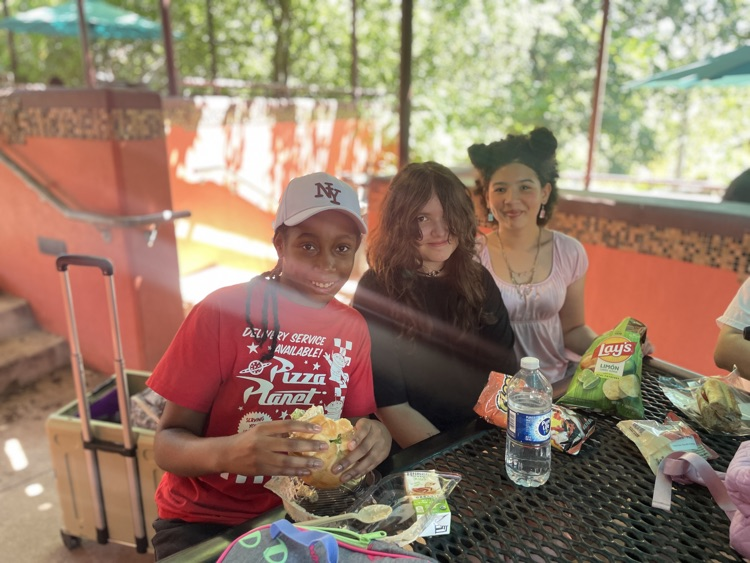 Three girls eating lunch at the zoo under an awning