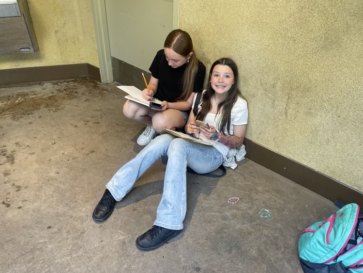 Two girls sitting on the floor against the wall, drawing gorilla sketches