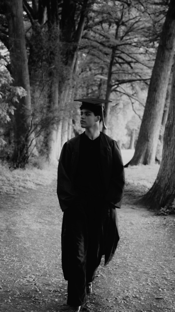 student in cap and gown walking by trees